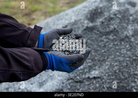 Hands of a construction worker in blue gloves holding gravel, with a large pile of gravel visible in the background on a construction site Stock Photo