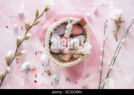 Easter decoration with pink and purple eggs with a bunny motif in a woven basket, decorated with magnolia flowers and willow branches, pink background Stock Photo