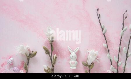 Star magnolia branches and flowers and a porcelain Easter bunny on a pink background, top view with copy space Stock Photo
