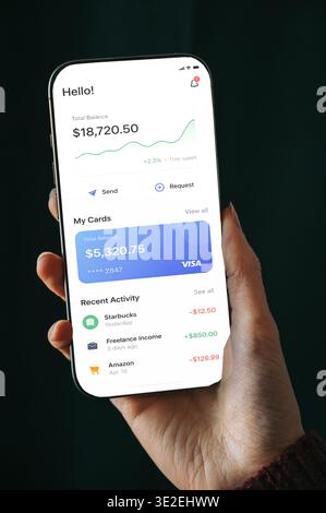 Riga, Latvia - March 19, 2026: Close-up of a hand holding a smartphone displaying a modern mobile banking app interface with balance, card details, an Stock Photo
