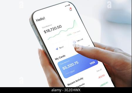 Riga, Latvia - March 19, 2026: Close-up of a person using a smartphone mobile banking app, tapping to send or request money. Screen shows balance, car Stock Photo