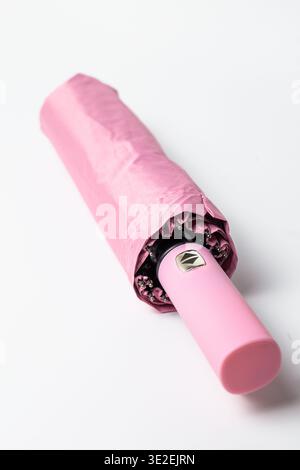 Compact pink umbrella with smooth fabric and ergonomic handle featuring intuitive buttons for instant opening-closing. Metallic body and waterproof ma Stock Photo