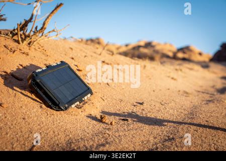 Rugged power bank with solar panel charging electricity in the nature and sand of the desert during a sunny day. Outdoor adventure ensuring charging Stock Photo