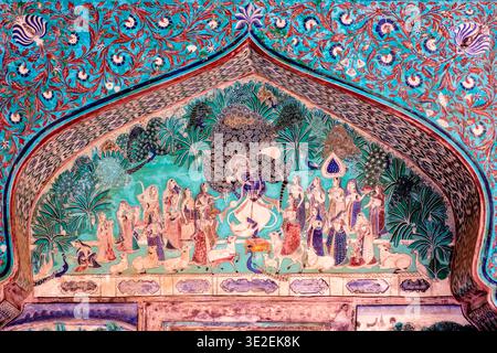 A detailed mural in the Chitrashala of Bundi depicts Lord Krishna dancing with gopis surrounded by peacocks within an ornate arch. Stock Photo