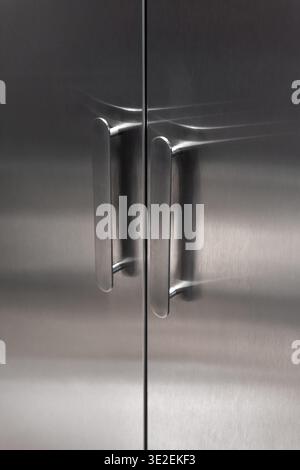 Stainless steel cabinet doors with modern oval handles. Close-up of sleek, metal double doors featuring minimalist silver handles - industrial design. Stock Photo