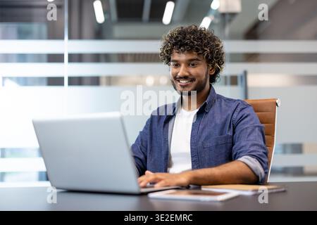 Portrait of a young Muslim man sitting in the office at a desk and working on a laptop. Stock Photo