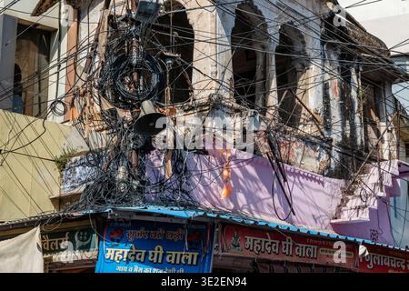 A chaotic tangle of overhead power lines and cables hangs precariously above shops with colourful Hindi signage in the town of Bundi. Stock Photo