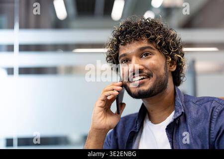 Close-up photo of a smiling Indian man in an office talking on a mobile phone. Stock Photo