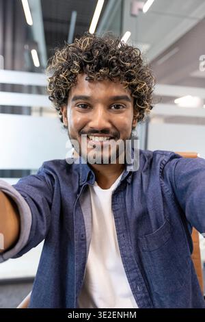 Vertical photo of a portrait of a young Indian man in an office, holding and talking to the camera. Stock Photo