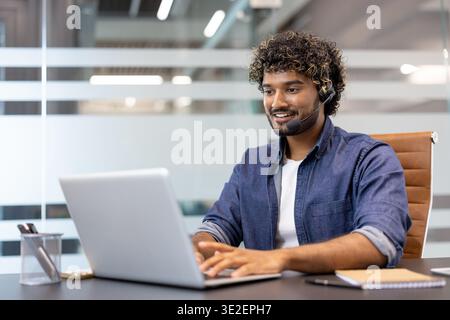 Young Indian man in headset working focused in office at laptop. Stock Photo