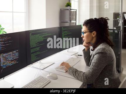 Woman software engineer coding at triple monitor setup in modern bright office Stock Photo