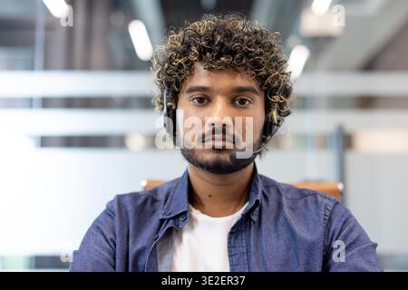 Close-up portrait of a young Indian man wearing a headset standing indoors and looking seriously at the camera. Stock Photo