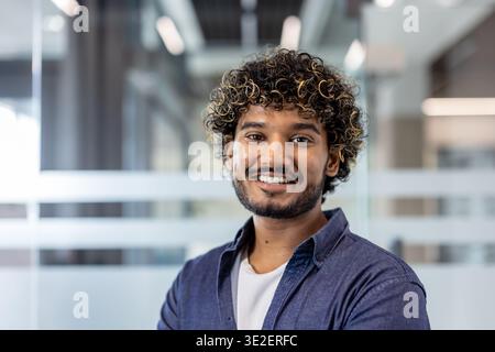 Close-up portrait of a young Indian man in a shirt who is in the office, standing and smiling at the camera. Stock Photo