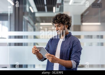 Young Indian man standing in office wearing shirt and using tablet. Stock Photo