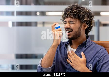 Indian young man using inhaler at workplace. Stock Photo