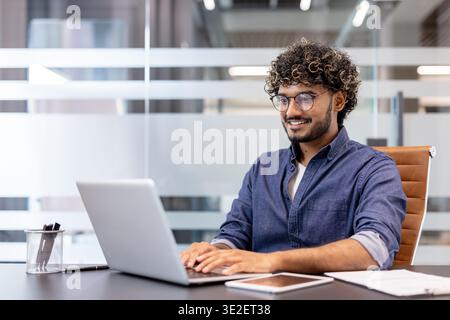 Smiling Indian man working in the office at a laptop. Stock Photo
