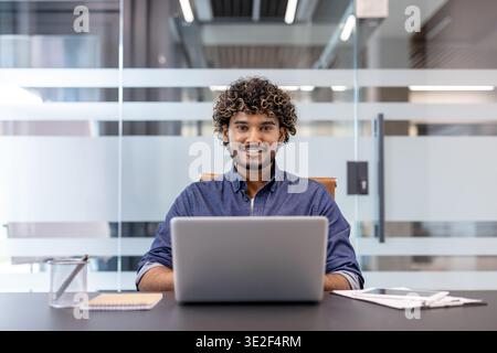 Portrait of a smiling young Indian man working in an office with a notebook and looking at the camera. Stock Photo