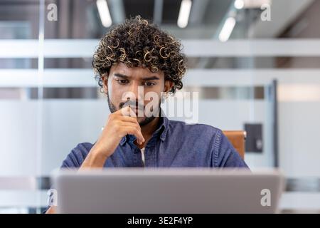 Thoughtful and focused young Indian man working in the office on a laptop. Stock Photo