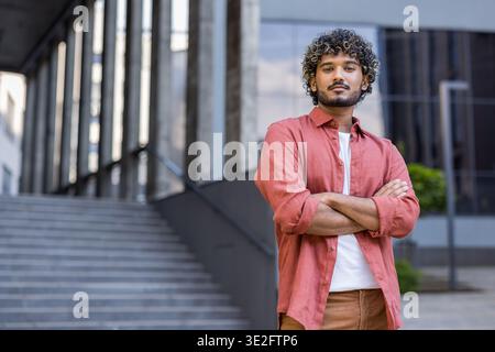 Smiling young Muslim man standing outside a building, arms crossed over chest and looking at camera. Stock Photo