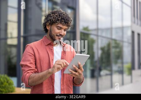 Indian young man in red shirt standing on the street and using tablet. Stock Photo