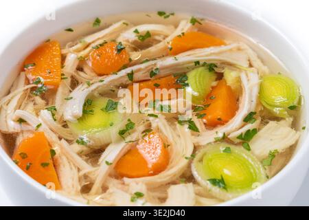 Homemade chicken soup in white bowl with carrots and celery isolated on white background Stock Photo