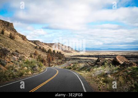 A two-lane road winds through a semi-arid mountain scene. Stock Photo