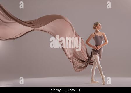 Young ballerina posing with flowing beige fabric in studio Stock Photo