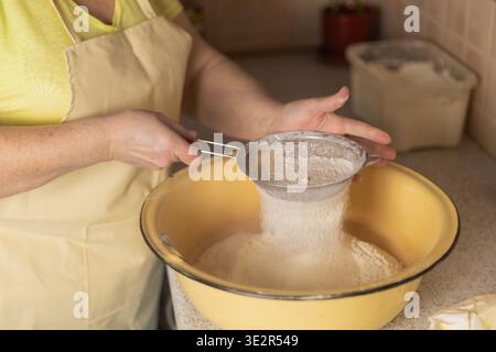 Adult woman hands sifting flour over bowl with sieve in kitchen Stock Photo