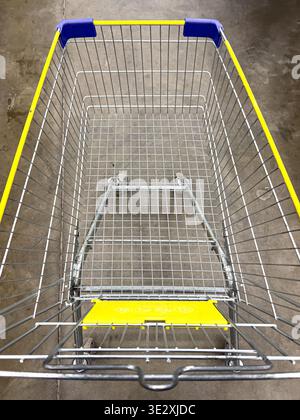 Empty metal shopping cart with yellow and blue details on a concrete surface Stock Photo
