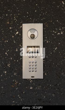 Modern intercom system with numeric keypad and camera integrated into dark textured wall near an entrance. Home security, building access control Stock Photo