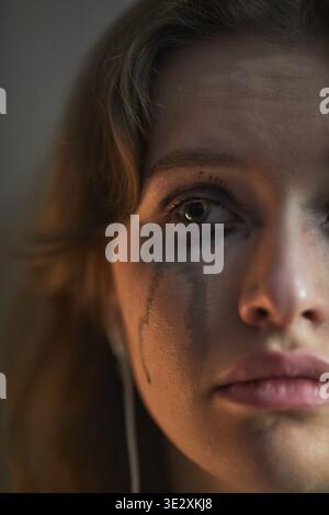 Vertical Portrait of young adult Caucasian woman looking into camera with tear-streaked face and smudged mascara, expressing intense sadness and vulnerability in close up composition Stock Photo