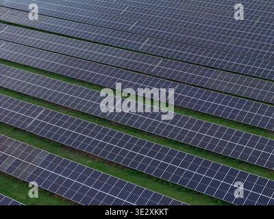 Aerial view shows solar panel rows on a green grass field highlighting renewable energy technology and sustainability. Stock Photo