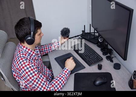 Man wearing headphones using a microphone and graphics tablet at his desk Stock Photo
