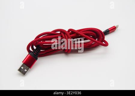 Red and black patterned smartphone charging cable with connector plugs, coiled for storage and on a white background Stock Photo
