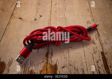 Red and black patterned smartphone charging cable with connector plugs, coiled for storage and on a wooden table Stock Photo