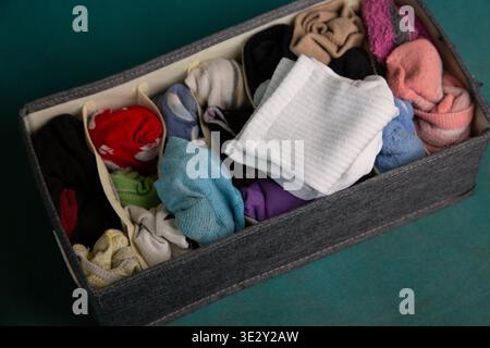 A box filled with various socks is placed on a green surface. The socks are different colors and designs. This scene shows organization and tidiness in a common household item. Stock Photo