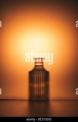 Glass bottle casting a dramatic silhouette against an ethereal orange and amber lit background, creating a minimalist composition with a serene and wa Stock Photo
