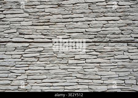 Neutral gray stacked stone wall with horizontal layers and rough rock texture Stock Photo