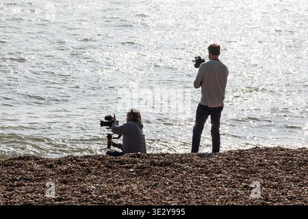 Two photographers in silhouette on a beach filming the sea. Stock Photo