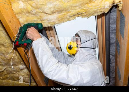 Man installing mineral wool insulation in an attic using a stapler Stock Photo