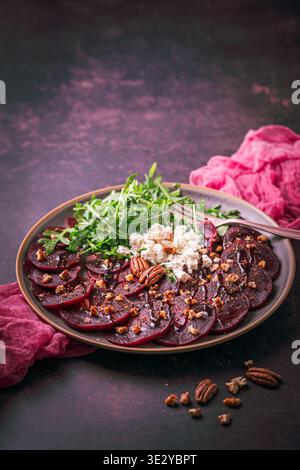 Beetroot carpaccio with balsamic glaze, walnuts, sheep cheese and rocket salat on dark background, vertical with copy space Stock Photo