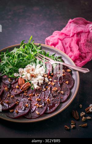 Beetroot carpaccio with balsamic glaze, walnuts, sheep cheese and rocket salat on dark background, vertical with copy space Stock Photo