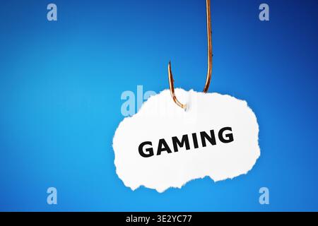 Conceptual image about the risk of Video Game Addiction and Internet Gaming Disorder. Piece of paper with printed word Gaming hanging on a fishing hoo Stock Photo
