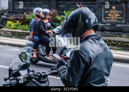 Motorcyclist Checking Smartphone on a Bali Street Indonesia Stock Photo