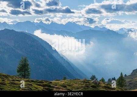 Majestic mountain range with clouds and sun rays illuminating the valley in the Italian Alps Stock Photo
