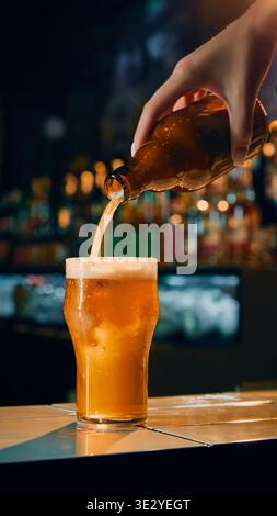 Beer being poured from bottle into glass on bar counter with foam forming. Stock Photo