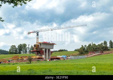 Concrete bridge pillar and tower crane under construction in a green rural landscape Stock Photo