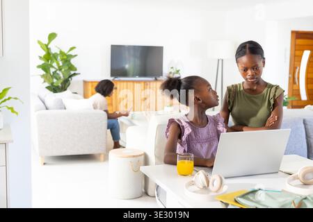 African American family gathering in bright living room, girls studying on laptop with orange juice Stock Photo