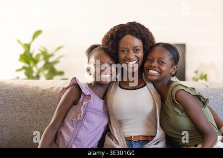 African mother with child and adolescent daughters sitting on gray sofa in living room, smiling Stock Photo