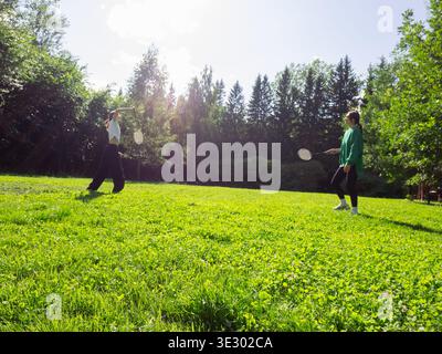 Mother and daughter playing badminton in summer park. Friends enjoying outdoor sports activity on sunny day. Healthy lifestyle, recreation and active Stock Photo